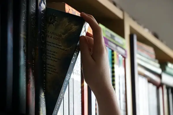 a person holding a book in front of a book shelf